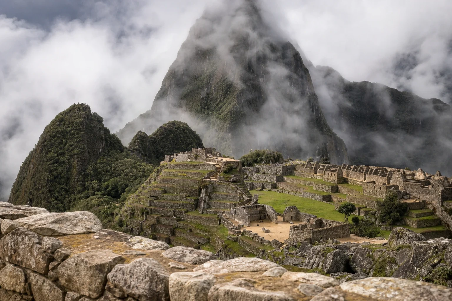 Blick über die Terrassen von Machu Picchu mit Nebel über den Anden